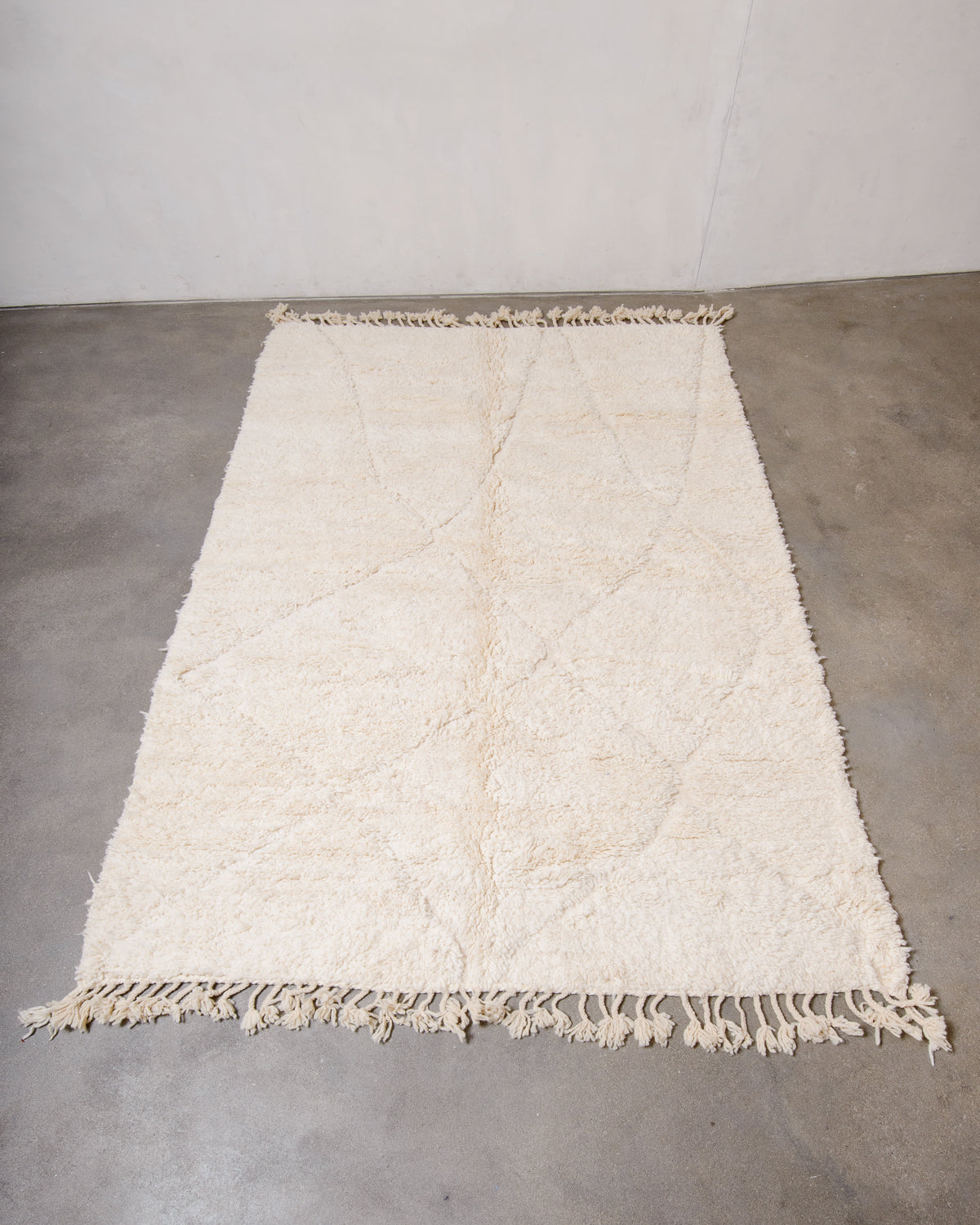 Cream wool Beniourain rug laying flat on concrete floor.